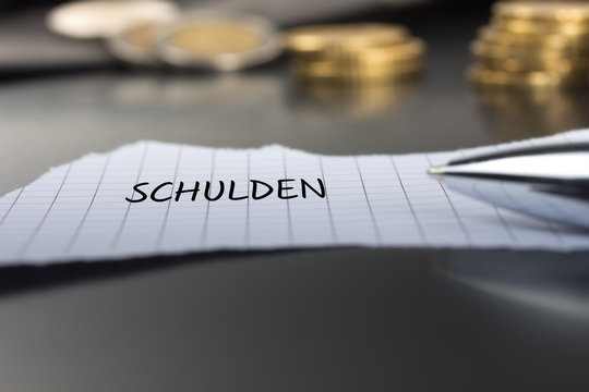 Schulden auf einem Zettel mit Stift vor Geldm&uuml;nzen