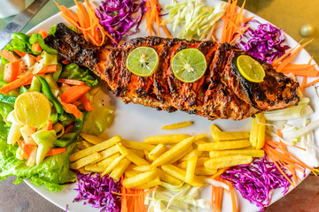 Spicy grilled fish served with crispy french fries and salad
