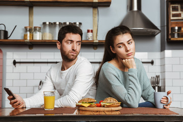 Unhappy young couple sitting at the kitchen