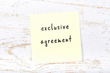 Yellow sticky note with handwritten text exclusive agreement