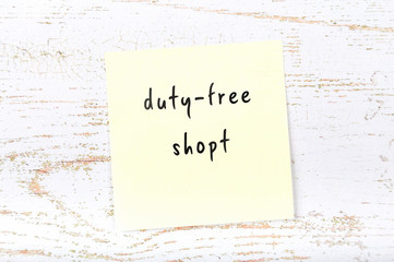 Yellow sticky note with handwritten text dutyfree shopt