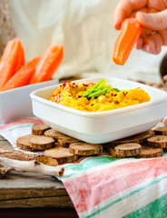 Classic hummus with herbs, olive oil in a ceramic bowl, served with carrot sticks. Vintage background. Traditional Middle Eastern cuisine. Hands of young woman. Eating process.