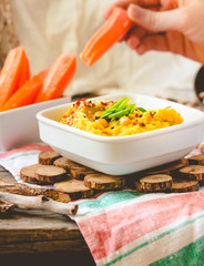 Classic hummus with herbs, olive oil in a ceramic bowl, served with carrot sticks. Vintage background. Traditional Middle Eastern cuisine. Hands of young woman. Eating process.Toning.