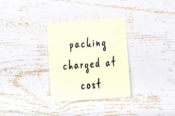 Yellow sticky note with handwritten text packing charged at cost