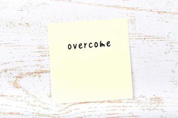 Yellow sticky note with handwritten text overcome