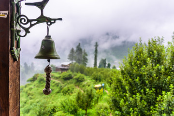 Beautiful Himalayan mountain landscape covered with monsoon clouds with old bell in foreground
