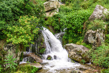 Fototapeta na wymiar Waterfall flowing through lush green mountain. Mountain river waterfall landscape. Waterfall river scene