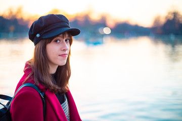 Portrait of young woman wearing stylish clothes on a lake at sunset in autumn-winter