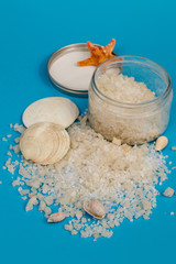 Large crystals of sea salt in a round transparent jar, next to seashells on a blue background. Selective focus.