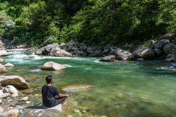 Man meditating yoga outdoor near the smooth flowing river with crystal clear water
