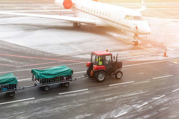 cargo freight tractor machine delivering luggage carts to airplane at airport. Airport carrier and service
