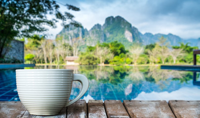 A white cup of coffee on the wooden table by the pool