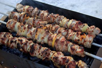 Tasty grilled meat on metal skewers on the brazier in winter. Roasted meat cooked at barbecue. BBQ fresh beef meat chop slices. Shashlik