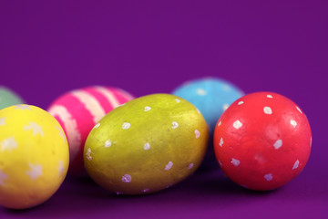 Easter background. Green, red and yellow painted eggs handmade on a purple background with bokeh. Cropped shot, close-up, nobody, horizontal, blurred, free space. Easter concept.