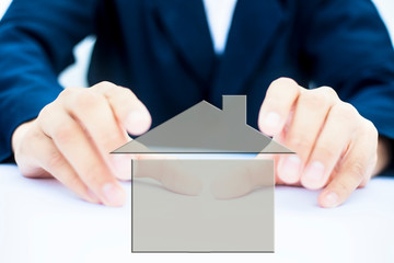 Close up of hands of business man or employee wearing blue colored suit isolated and holding a house dreaming or wishing to have such like it.