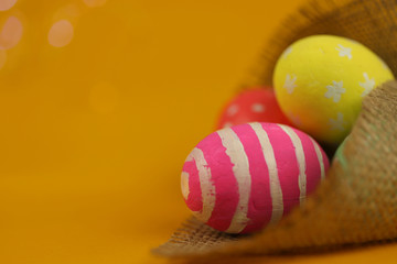 Easter background. Green, red and yellow painted eggs handmade in sackcloth on a yellow background with bokeh. Cropped shot, close-up, nobody, horizontal, blurred, free space. Easter concept.