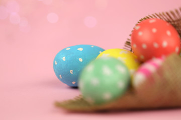 Fototapeta na wymiar Easter background. Green, red and yellow painted eggs handmade in sackcloth on a pink background with bokeh. Cropped shot, close-up, nobody, horizontal, blurred, free space. Easter concept.