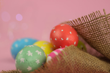 Easter background. Green, red and yellow painted eggs handmade in sackcloth on a pink background with bokeh. Cropped shot, close-up, nobody, horizontal, blurred, free space. Easter concept.