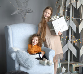 two little girls with gifts standing near a stylized Christmas tree