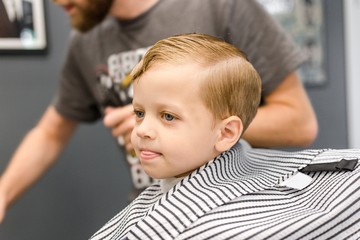 Baby blonde with blue eyes sitting in a chair in a Barber shop covered with a veil for hairdressing