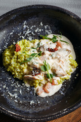  Risotto with porcini mushrooms, sauce, sun-dried tomatoes and pea sprouts on a beautiful clay deep dish of gray color