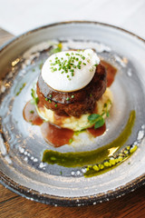  Meat cutlet on a pillow of mashed potatoes with poached egg on top, poured with pesto and teriyaki with meat sauce, decorated with green onions.