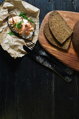 smoked salmon sandwich in Kraft paper on black wood background, top view, space for text