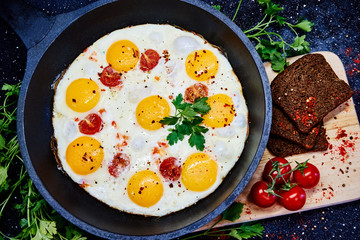 Fried eggs in a frying pan with cherry tomatoes and bread for breakfast on a black background.