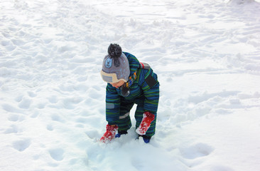 Fototapeta na wymiar A four-year-old child, a boy dressed in colorful winter clothes, plays with snow on a snowy ground on a sunny winter day.