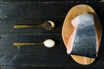 salmon on a wooden chopping Board, spoon with salt and pepper on black background, top view
