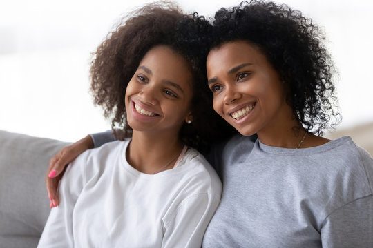 Happy young African American mom hug teenage daughter making picture together, smiling black mother and teen girl sit on couch posing for photo, parent and child embrace as best friends