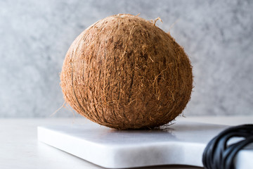 Fresh Organic Brown Raw Coconut on White Marble Board.