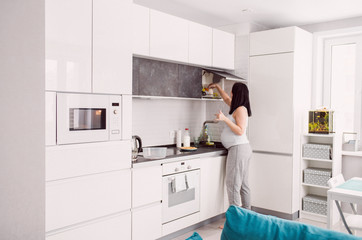 Young pregnant woman in the white kitchen at home maternity concept washing the dishes