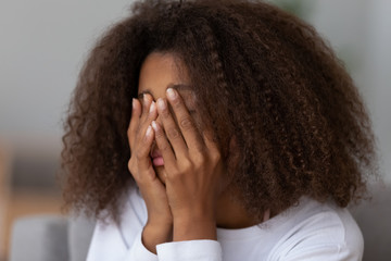 Close up of upset African American teenage girl cover face with hands, feel disappointed having...