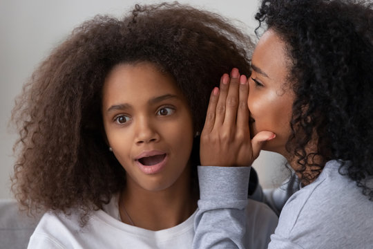 African American female tell secret to surprised girlfriend, black young mom or nanny spend time together with teenage girl, sharing or gossiping, modern parent and teen daughter best friends concept