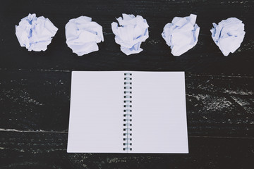 set of scrunched paper balls and empty notepad on dark moody background