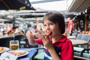 Cute child, boy, eating pizza in restaurant, happily smiling