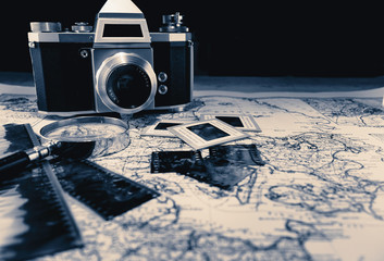 Old vintage camera on map with negatives, old pictures and a magnifier glass. Retro, nostalgic, photography concepts.
