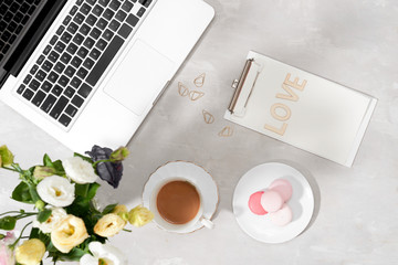 Feminine flat lay workspace with laptop, cup of tea, macarons, Love letter and flowers on white table. Top view mock up.