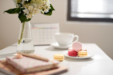 Office table desk. Feminine desk workspace frame with calendar, diary, hortensia bouquet, macaron and coffee on white background. ideas, notes or plan writing concept