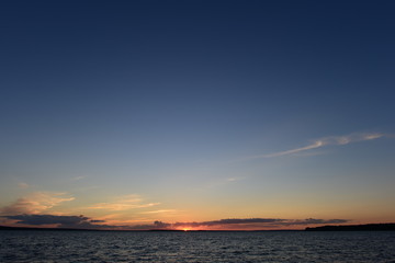Sunset is a small bright point on the horizon the sun is infinite in space the blue of the sky and the water of the lake