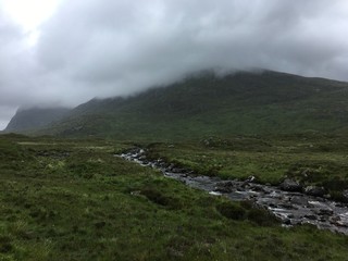 A scenic mountain footpath with a stream and a very stormy sky