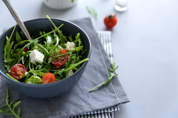 Bowl of arugula salad with tomatoes and feta sheese on gray wooden background. Vegetarian food concept