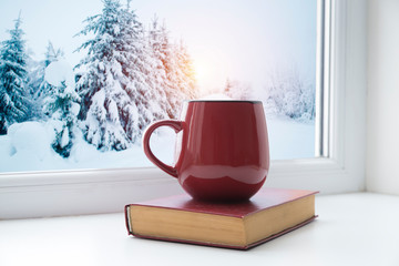 Obraz na płótnie Canvas Winter background - cup with candy cane, woolen scarf and gloves on windowsill and winter scene outdoors. Still life with concept of spending winter time at cozy home with cold weather outdoors