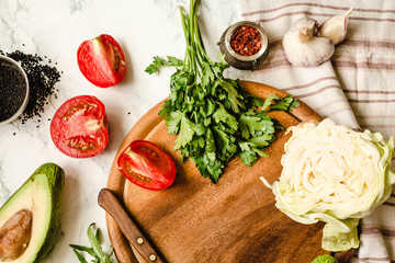 Greens, tomatoes, cucumbers, spices, avocados, vegetables, spring fresh food. Preparing raw salad. Wooden board, top view, place for text.Clean eating diet. Diet food concept. Healthy food background.