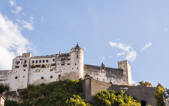 Burg auf Berg mit weisser Burgmauer und T&uuml;rmen vor blauem Himmel mit Wolken