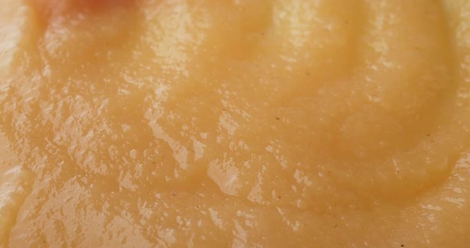 Close video of applesauce being stirred with a red plastic spoon on a white plate illuminated with natural light.