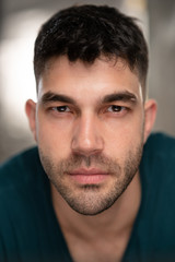 Handsome caucasian white male with black short hair and stubble with blue t shirt serious