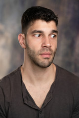 Obraz premium Handsome caucasian white male with black short hair and stubble with brown t shirt, looking worried