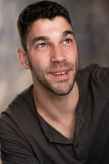 Fototapeta premium Handsome caucasian white male with black short hair and stubble with brown t shirt feeling optimistic